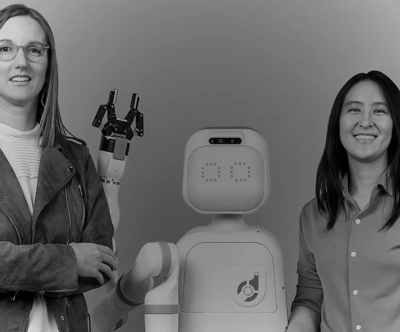 Diligent Robotics’ two co-founders standing either side of Moxi.
