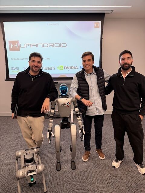 Exequiel Barrirero of binbash standing with Humandroid’s founders, beside a Humandroid humanoid and a quadruped robot, in front of a slide listing AWS, binbash and NVIDIA.